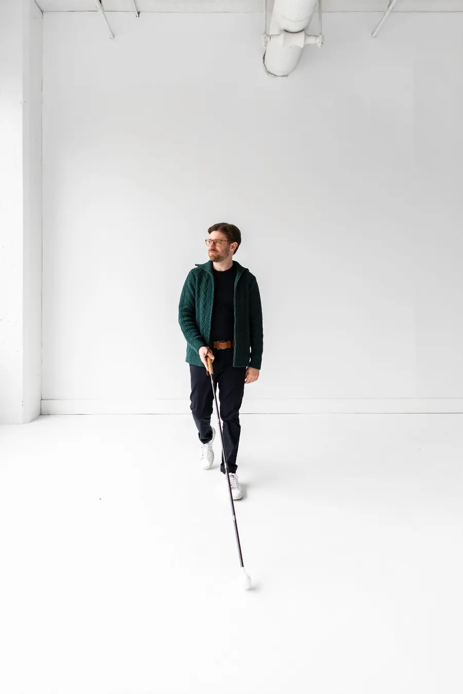 Charlie standing in a bright studio space, holding a white cane, wearing a green cardigan.